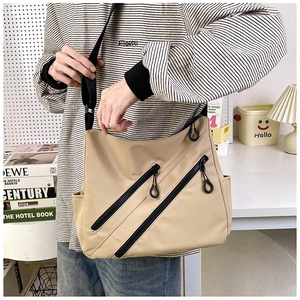 Detail of khaki multi-pocket tote bag with black diagonal zippers and wide shoulder strap