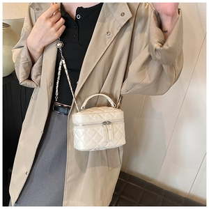 Close-up of beige quilted leather mini box bag with silver chain strap worn with a trench coat