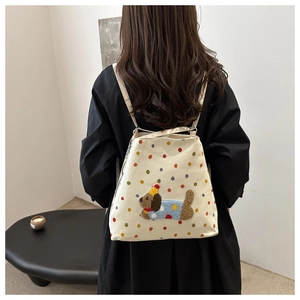 Vue détaillée du sac à dos en toile blanche avec pois colorés et écusson de chien en peluche