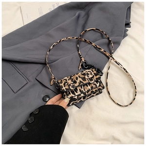 Detail of leopard print crossbody bag with decorative buckles and resin chain on suit