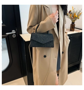Détail d'une pochette de soirée noire pailletée avec chaîne dorée tenue par un mannequin