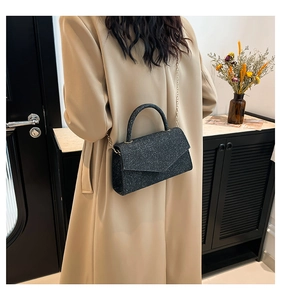 Gros plan d'un sac bandoulière noir texturé avec chaîne dorée et poignée porté par un mannequin