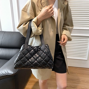 Minimalist black quilted tote bag in glossy patent leather held by a model in a trench coat
