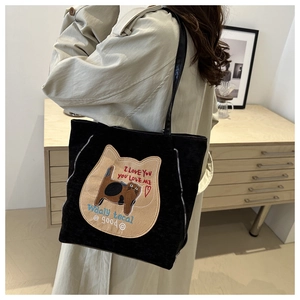 Close-up of black corduroy tote bag featuring a cute cat patch and silver zipper detail