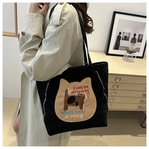 Close-up of black fabric tote bag with cat embroidery and silver zipper details on shoulder