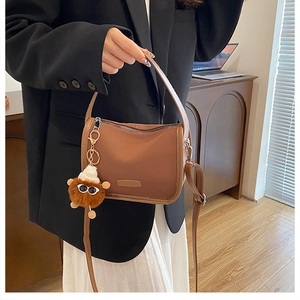 Detailed close-up of brown nylon pillow bag with cute plush pendant and shoulder strap