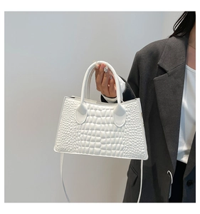 Detail of white crocodile pattern handbag with dual handles and structured trapezoid shape