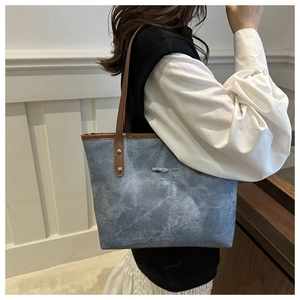 Dettaglio della borsa tote in denim blu con lavaggio vintage e tracolla in pelle marrone