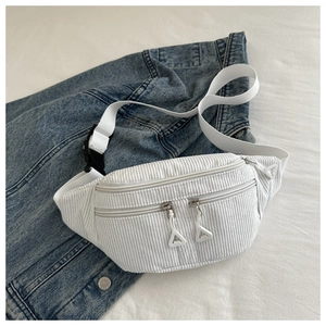 Detail of white corduroy waist bag with multiple zippers over a blue denim jacket