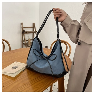 Detail of blue denim tote bag with black leather straps and decorative bow detail
