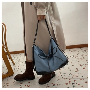 Detail of blue denim tote bag with leather trim and delicate bowknot on soft shoulder bag