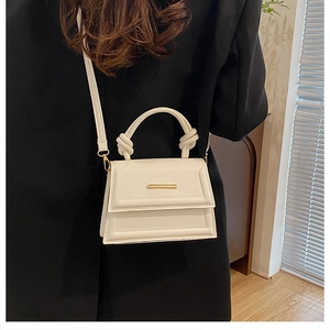 Close-up of white leather handbag with gold metal clasp and knotted handle detail