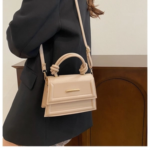 Detail of beige leather small square bag with knot handle and gold hardware on model