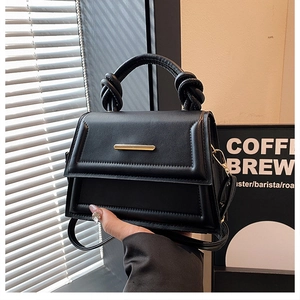 Detail view of the knotted handle and golden metal clasp on a black leather handbag