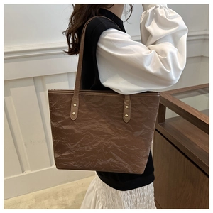 Detail of dark brown tote bag featuring unique pleated texture and gold rivet hardware