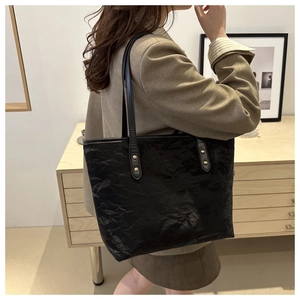 Side view of black tote bag with glossy pleated texture and gold rivet details on shoulder strap