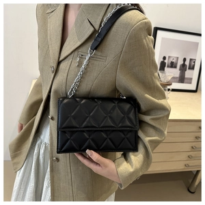 Detail of black quilted leather shoulder bag with silver chain strap on brown suit