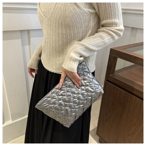 Détail d'une pochette argentée matelassée à motif de cœur tenue par un mannequin