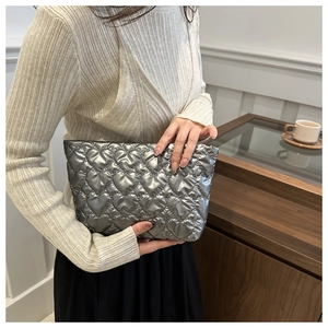 Gros plan sur la pochette argentée à surpiqûres en cœur tenue par un mannequin en intérieur