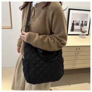 Close-up of black quilted tote bag with diamond stitching and shoulder strap details