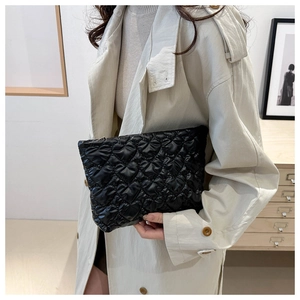 Détail d'une pochette noire matelassée en cœur tenue par un mannequin au style moderne