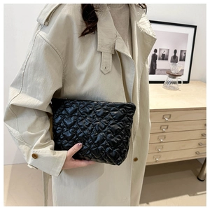 Détail d'une pochette noire à matelassage cœur portée avec un manteau beige élégant