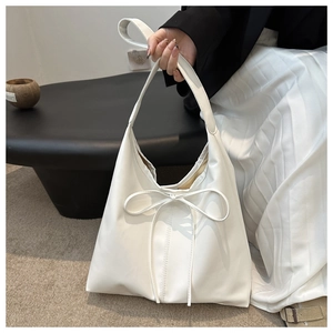Detail of a creamy white hobo bag with an elegant bow and soft pleated leather texture