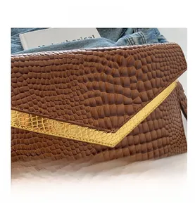 Close-up of brown crocodile pattern envelope clutch with golden V-shaped metal trim