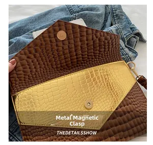 Detail of brown crocodile pattern envelope clutch featuring dual golden magnetic snap closures