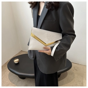Detail of white crocodile embossed envelope clutch featuring a gold V-shaped metal trim