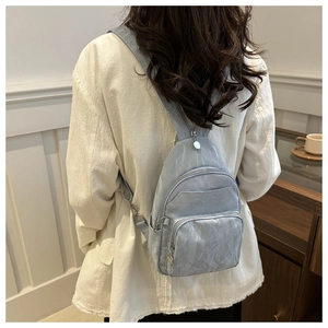 Detail of light blue nylon sling bag with multiple zippers shown on a model's back
