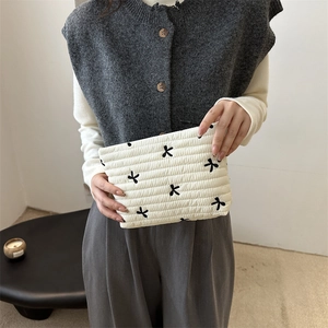 Quilted white cosmetic bag with black bow embroidery held by a model in a minimal setting