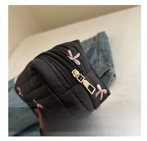 Close-up of smooth gold metal zipper on black quilted makeup bag with pink bow embroidery