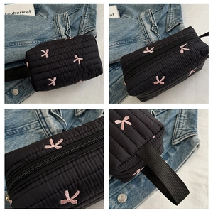 Macro view of black quilted pencil case with pink bow embroidery and zipper details