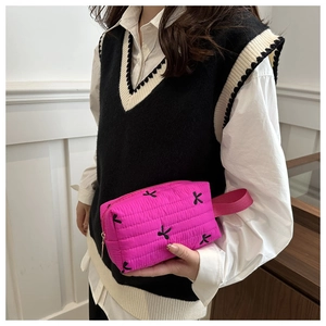 Detail of rose red quilted cosmetic bag featuring black bow embroidery and fabric handle
