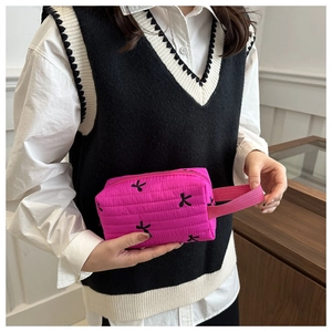 Close-up of pink quilted cosmetic bag featuring black bow embroidery and side handle strap