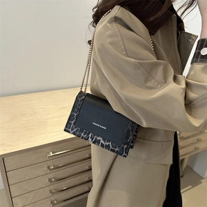 Chic leopard print chain square bag in black leather worn with a beige trench coat