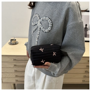 Close-up of black quilted clutch with pink bow embroidery and side wristlet strap
