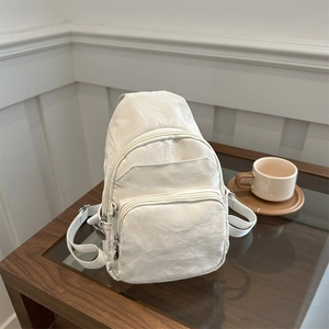 Minimalist white pleated sling bag with adjustable strap on a modern glass table
