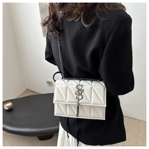 Close-up of quilted cream white shoulder bag with S-logo, fringe detail and chain strap