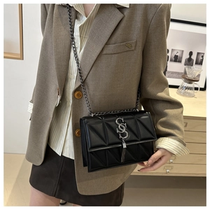 Close-up of black quilted crossbody bag with silver S-buckle and metal tassel on model