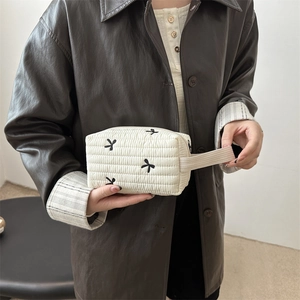 Quilted cream pencil case with black bow patterns and a side handle carried by a model