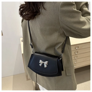 Close-up of black matte leather saddle bag with silver bow accent on green blazer
