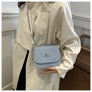 Détail du sac selle plissé bleu clair avec une boucle papillon argentée sur un manteau