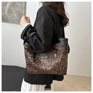 Leopard print tote bag with black faux leather straps shown from a side-carrying perspective