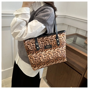 Detail of leopard print tote bag featuring black leather handles and gold rivet accents