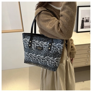 Detail of leopard print tote bag featuring black leather straps and gold rivet accents