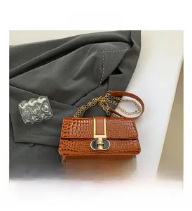 Detail of dark brown croc-embossed shoulder bag with golden chain on grey blazer