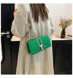 Detail of green faux crocodile leather bag with gold chain strap and metal T-lock