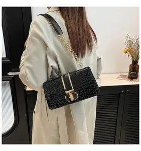 Detail of black crocodile texture shoulder bag with gold chain strap and metal buckle